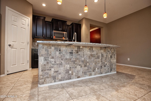 kitchen featuring hanging light fixtures, light tile patterned floors, light stone countertops, and a center island with sink