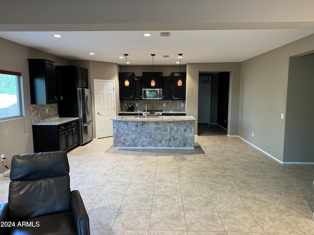 kitchen featuring hanging light fixtures, light stone countertops, appliances with stainless steel finishes, and a center island with sink