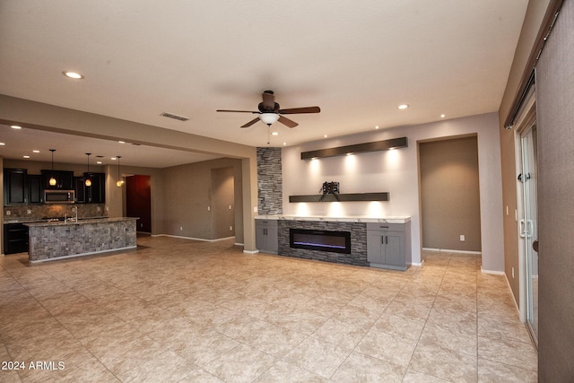 unfurnished living room featuring a stone fireplace and ceiling fan