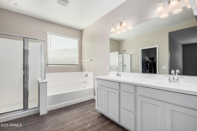 full bath featuring wood finish floors, a garden tub, double vanity, a stall shower, and a sink