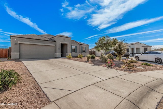 view of front of property featuring a tile roof, stucco siding, fence, a garage, and driveway