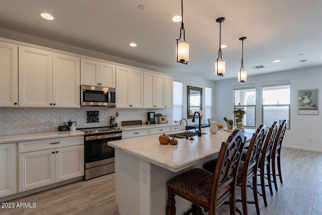 kitchen with a breakfast bar, white cabinets, hanging light fixtures, stainless steel appliances, and a center island with sink