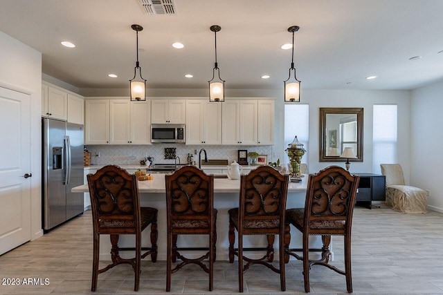 kitchen featuring pendant lighting, white cabinetry, stainless steel appliances, an island with sink, and a kitchen bar