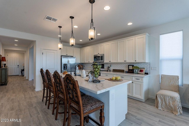 kitchen featuring stainless steel appliances, white cabinetry, visible vents, a kitchen breakfast bar, and backsplash