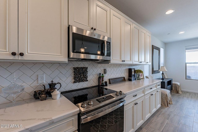 kitchen with tasteful backsplash, appliances with stainless steel finishes, light stone countertops, and white cabinets