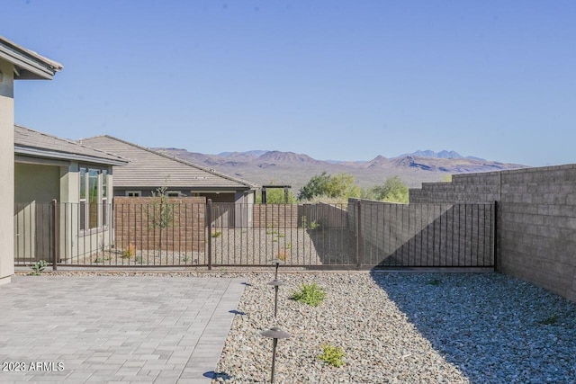 view of gate with a fenced backyard, a mountain view, and a patio