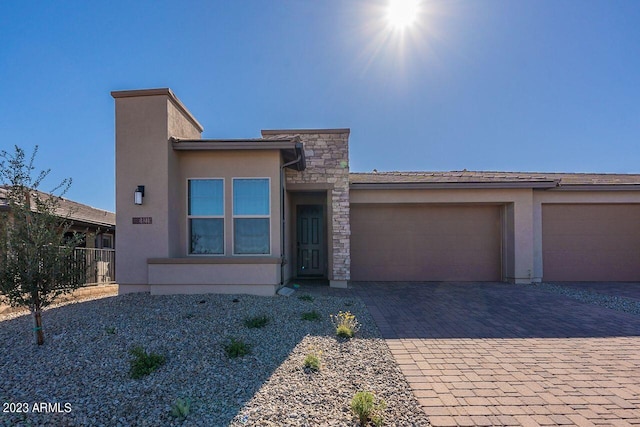 view of front of house featuring decorative driveway, stucco siding, fence, a garage, and stone siding