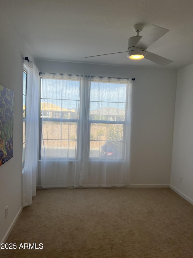 spare room with a ceiling fan, light carpet, and baseboards