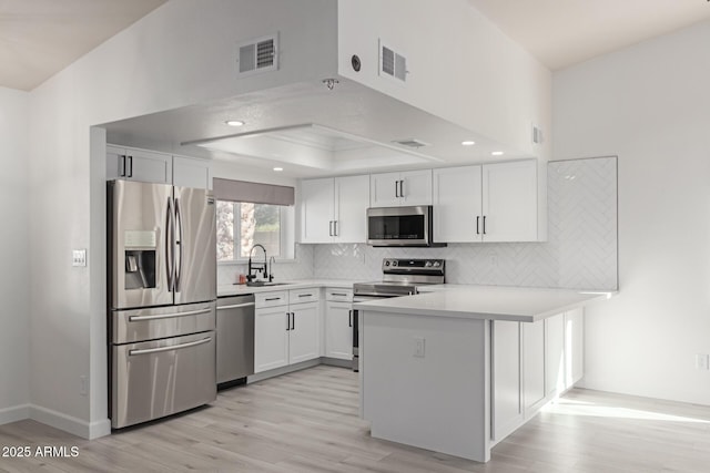 kitchen with sink, white cabinetry, appliances with stainless steel finishes, kitchen peninsula, and a raised ceiling