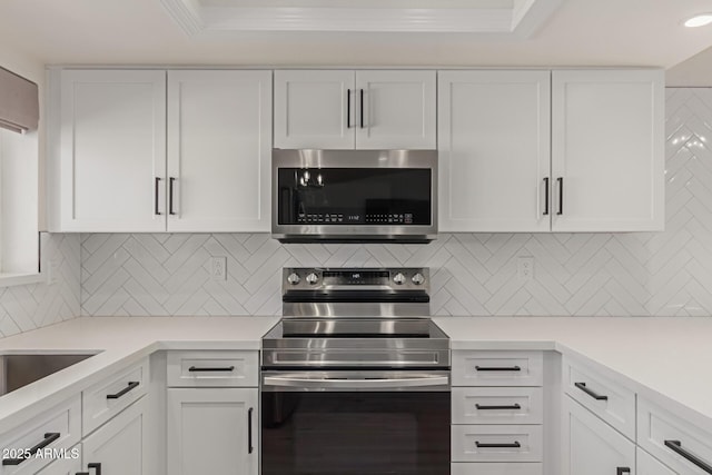 kitchen with white cabinets, stainless steel appliances, ornamental molding, and backsplash