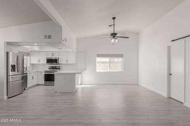 kitchen with sink, ceiling fan, appliances with stainless steel finishes, white cabinets, and a barn door