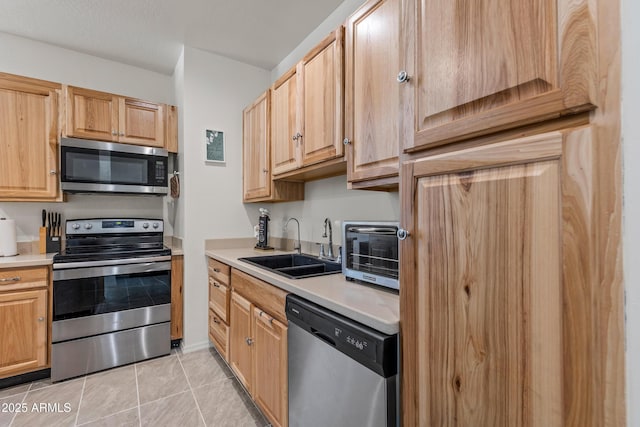 kitchen with light brown cabinets, light tile patterned flooring, a sink, light countertops, and appliances with stainless steel finishes