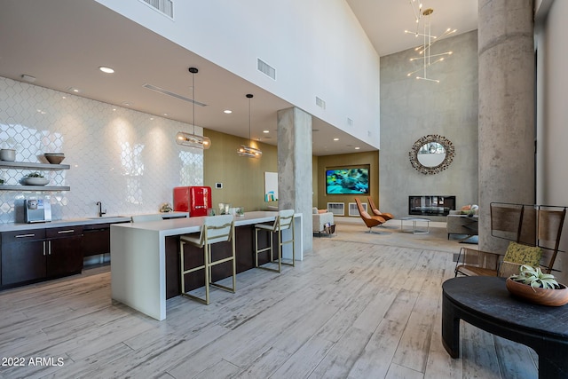 kitchen with backsplash, light wood-type flooring, dark brown cabinetry, a breakfast bar area, and decorative columns