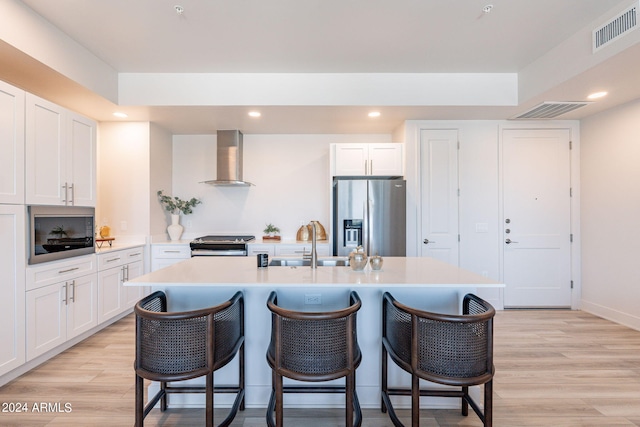 kitchen with white cabinets, wall chimney range hood, stainless steel appliances, and light hardwood / wood-style flooring