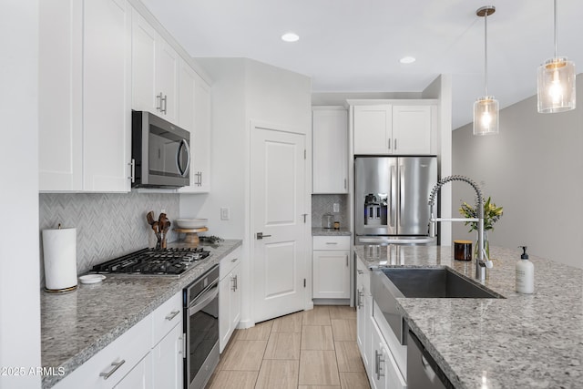 kitchen featuring stainless steel appliances, a sink, white cabinets, backsplash, and decorative light fixtures