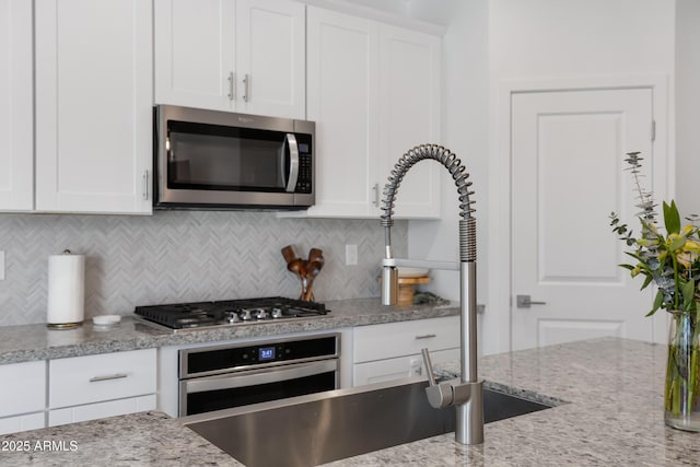 kitchen with light stone counters, white cabinetry, stainless steel appliances, and decorative backsplash