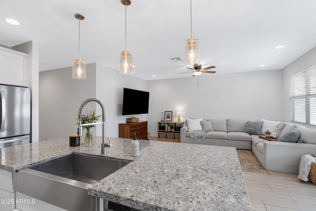 kitchen with a sink, visible vents, white cabinets, open floor plan, and hanging light fixtures