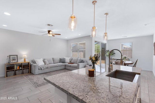 kitchen featuring a center island with sink, visible vents, light stone countertops, a sink, and recessed lighting