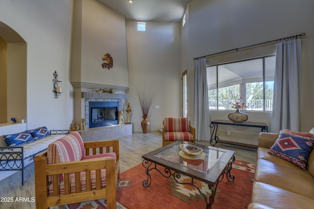 living room with light wood-type flooring, a fireplace, and a towering ceiling