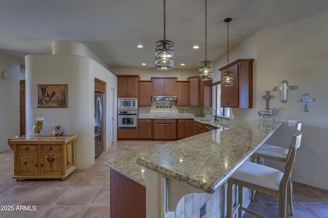 kitchen featuring pendant lighting, sink, a kitchen bar, kitchen peninsula, and stainless steel appliances