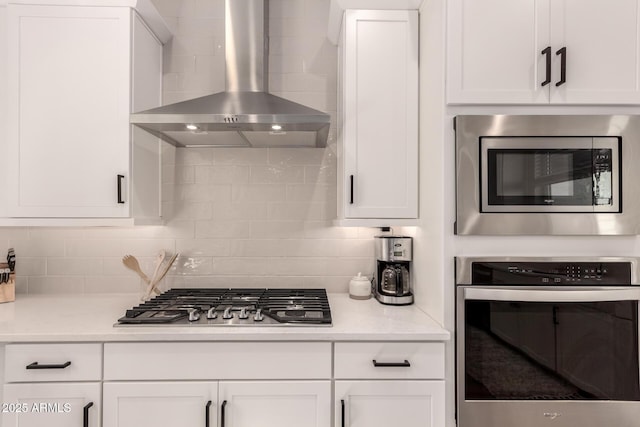 kitchen featuring tasteful backsplash, white cabinets, appliances with stainless steel finishes, light countertops, and wall chimney range hood