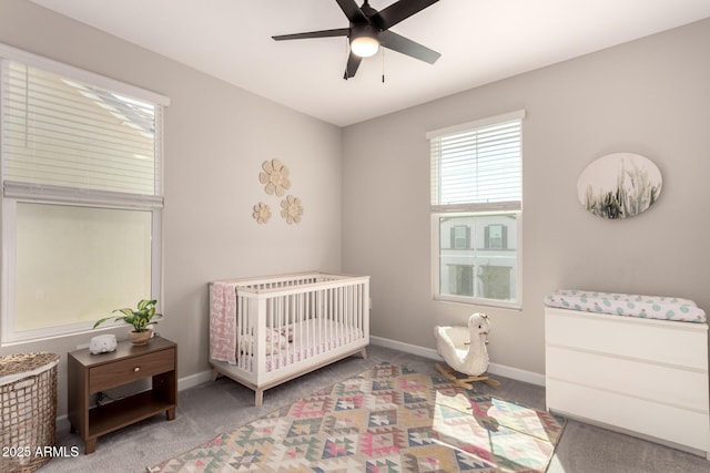 carpeted bedroom featuring a crib, baseboards, and a ceiling fan