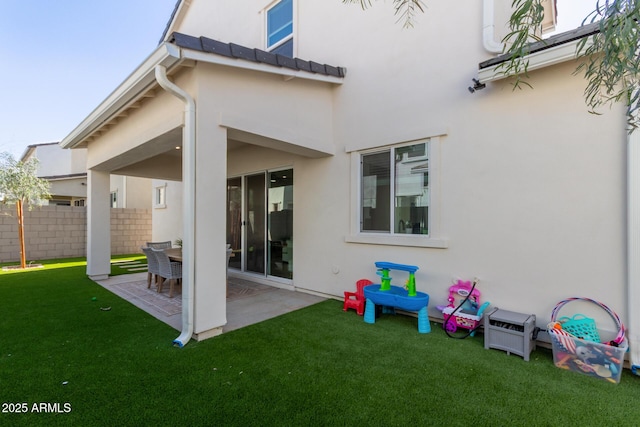 rear view of house featuring a patio, a tiled roof, fence, a yard, and stucco siding