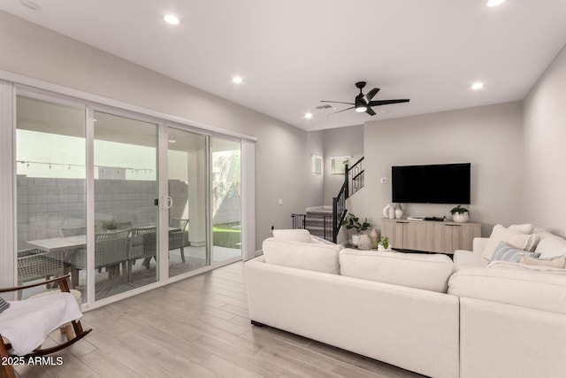 living room featuring a ceiling fan, recessed lighting, light wood-style flooring, and stairs