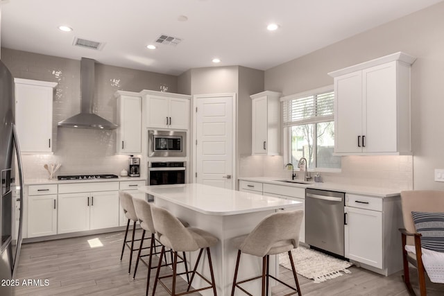 kitchen featuring appliances with stainless steel finishes, a kitchen breakfast bar, visible vents, and wall chimney exhaust hood