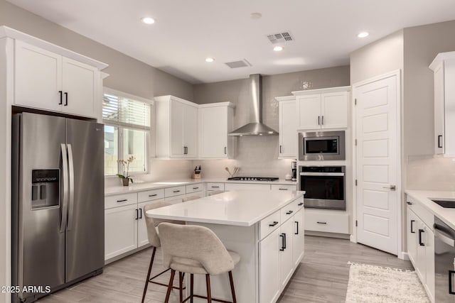 kitchen featuring visible vents, appliances with stainless steel finishes, white cabinetry, a kitchen island, and wall chimney exhaust hood