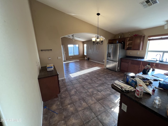 kitchen featuring lofted ceiling, sink, stainless steel fridge, hanging light fixtures, and ceiling fan with notable chandelier