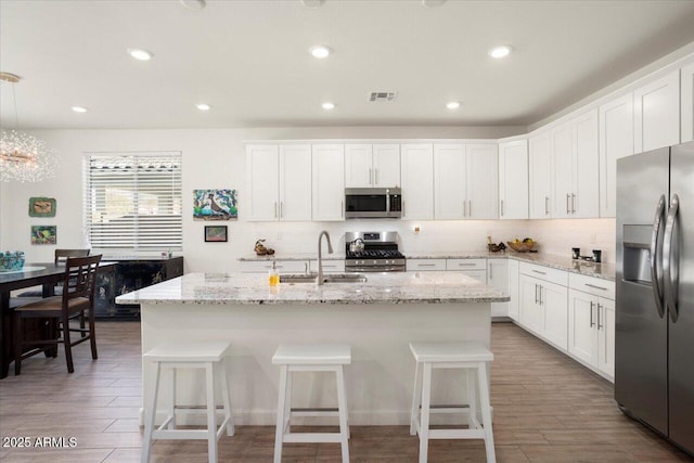 kitchen with pendant lighting, sink, white cabinetry, stainless steel appliances, and a center island with sink