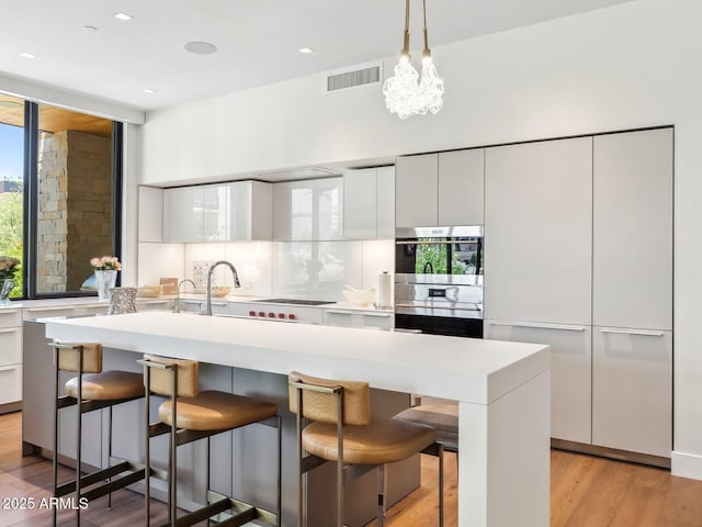 kitchen featuring modern cabinets, white cabinets, light wood-style floors, tasteful backsplash, and light countertops