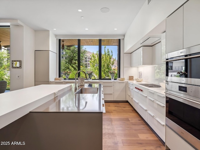 kitchen with a sink, appliances with stainless steel finishes, white cabinetry, light wood-style floors, and light countertops