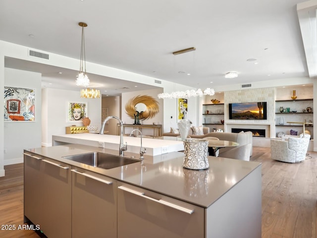 kitchen featuring a sink, a center island with sink, light wood-type flooring, decorative light fixtures, and open floor plan