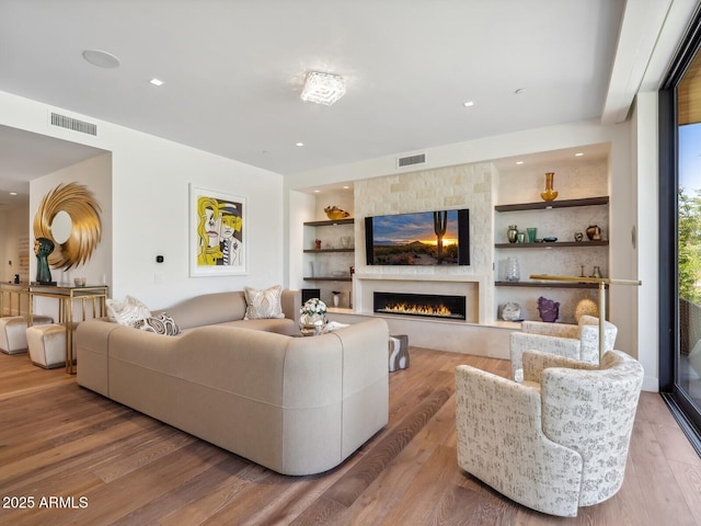 living area with a large fireplace, built in features, wood finished floors, and recessed lighting