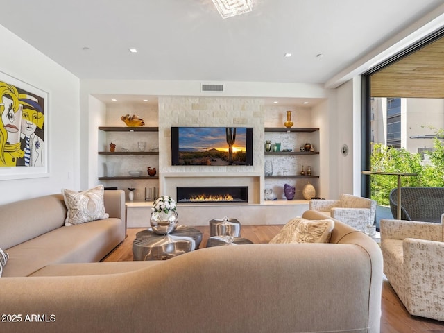 living room with built in shelves, wood finished floors, a large fireplace, and recessed lighting