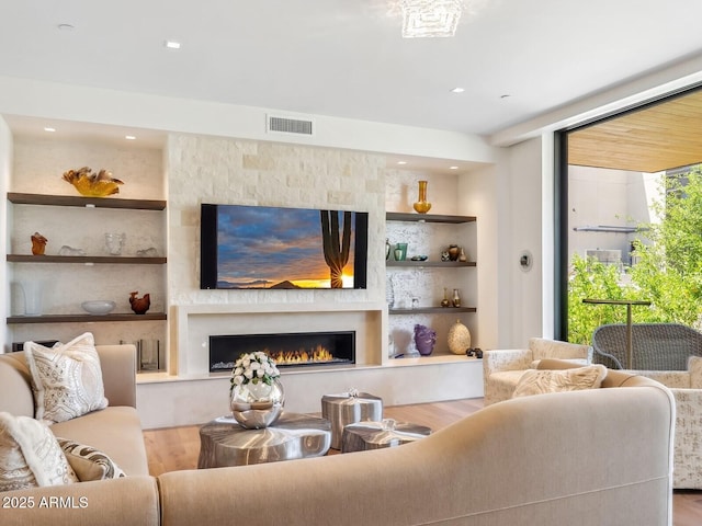 living room with wood finished floors, a lit fireplace, recessed lighting, and built in features