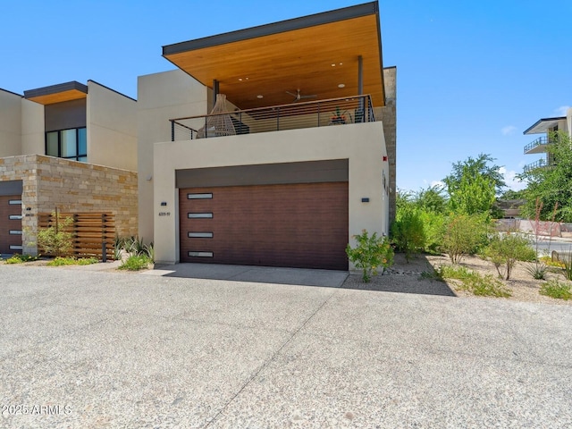 contemporary house featuring driveway, stucco siding, a balcony, and a garage