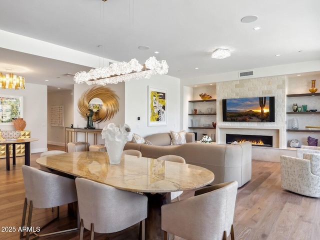 dining area with built in features, light wood-style flooring, a large fireplace, baseboards, and recessed lighting