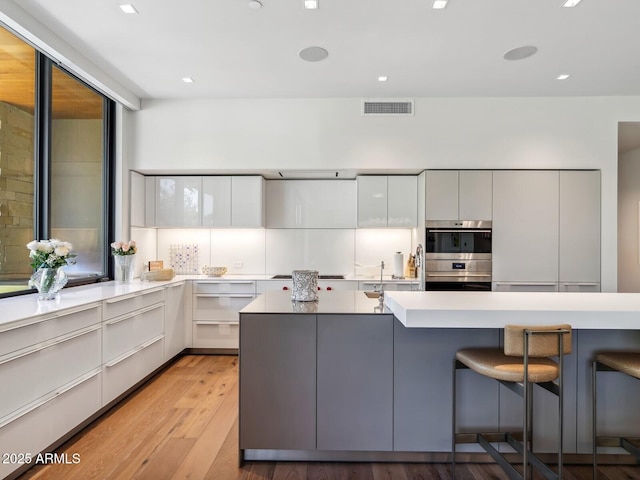 kitchen with modern cabinets, a kitchen bar, light wood-style flooring, white cabinetry, and appliances with stainless steel finishes