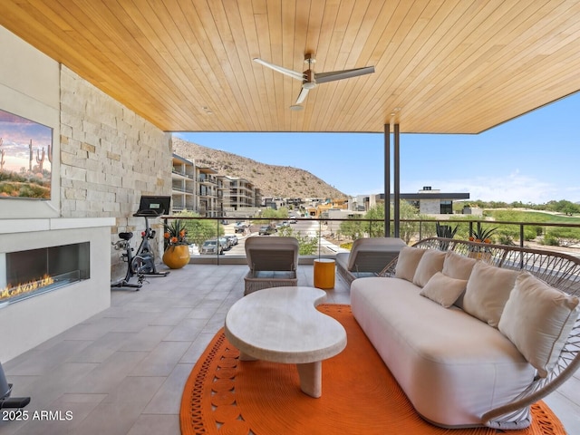 view of patio featuring a mountain view, an outdoor living space with a fireplace, and a ceiling fan