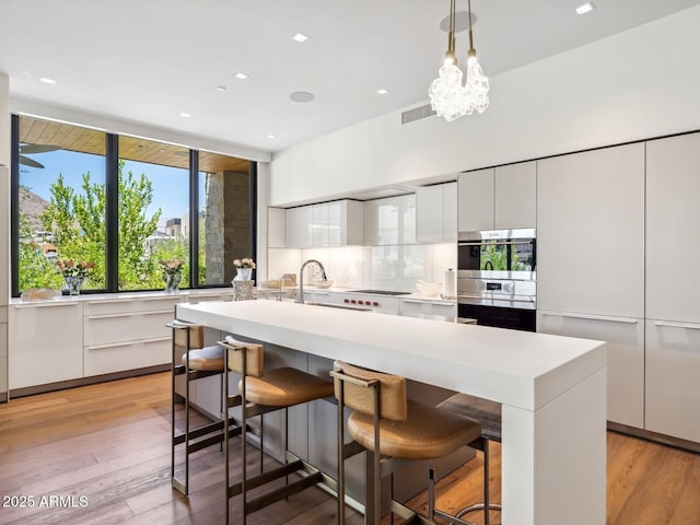 kitchen featuring modern cabinets, a sink, white cabinetry, light countertops, and a breakfast bar area