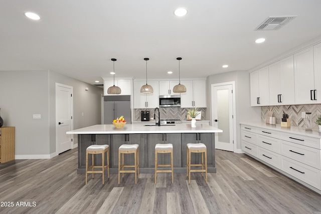 kitchen featuring white cabinetry, hanging light fixtures, stainless steel appliances, and a large island with sink