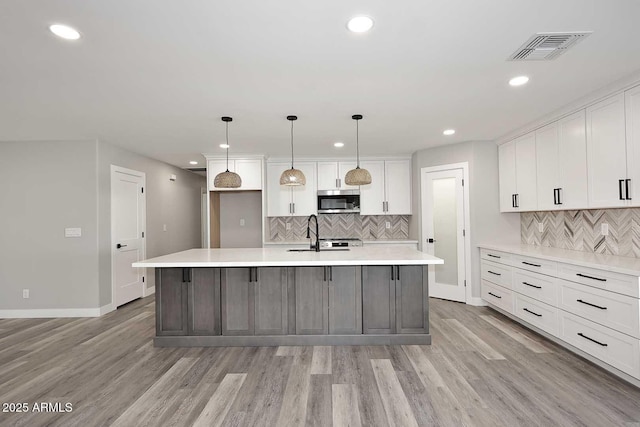 kitchen featuring sink, light hardwood / wood-style flooring, white cabinetry, decorative light fixtures, and a large island with sink