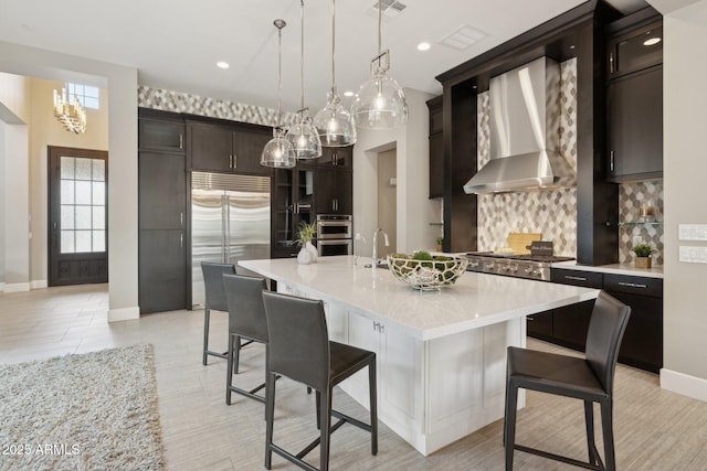 kitchen with stainless steel appliances, a breakfast bar, wall chimney exhaust hood, and light countertops