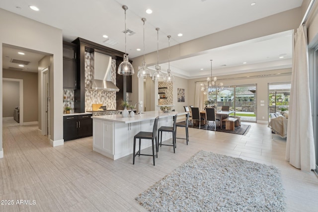 kitchen featuring visible vents, light countertops, backsplash, wall chimney range hood, and a kitchen breakfast bar