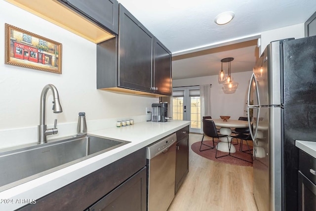 kitchen featuring stainless steel appliances, dark brown cabinets, hanging light fixtures, sink, and light hardwood / wood-style flooring