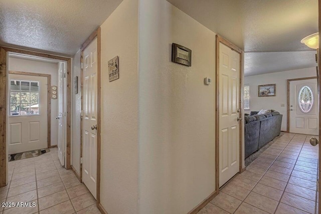 corridor with light tile patterned floors, a wealth of natural light, and a textured ceiling