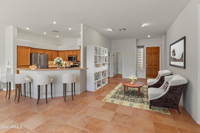 interior space with appliances with stainless steel finishes, kitchen peninsula, light tile patterned flooring, and a kitchen bar